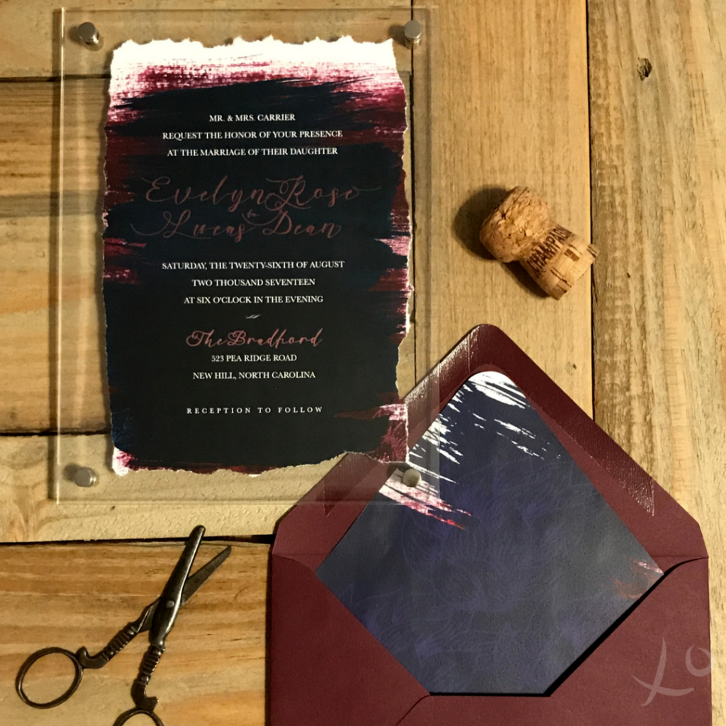 an bold maroon and navy wedding invitation with a deckled edge in an acrylic frame