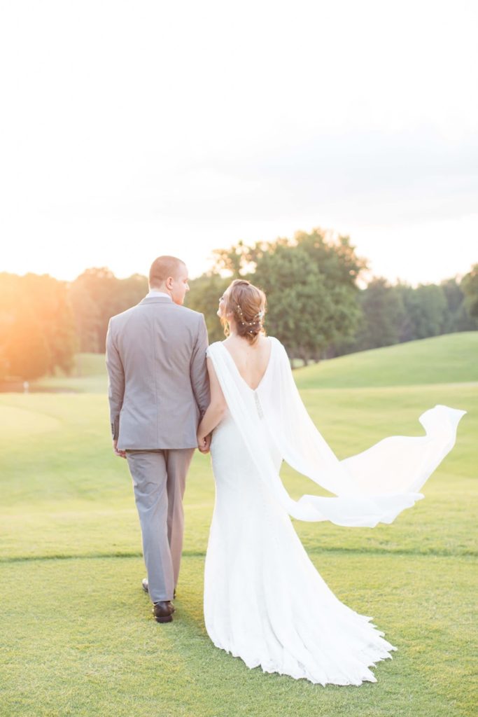 elegant bride with cape walks into horizon with groom