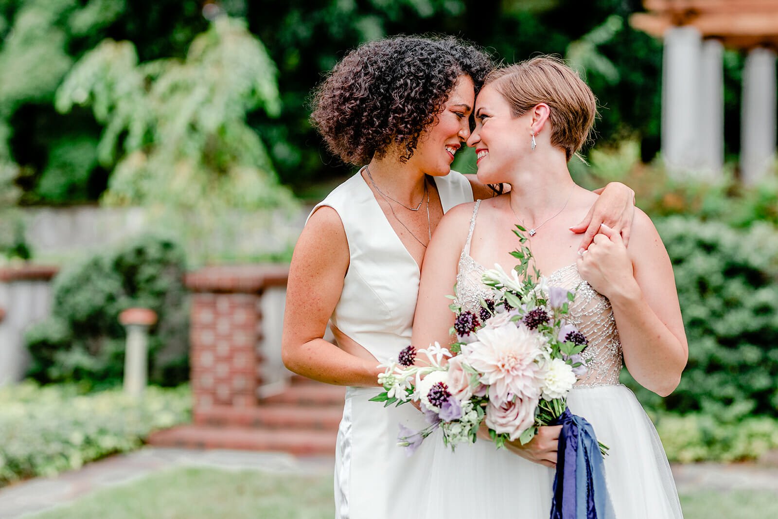 two brides pose nose to nose for wedding portrait holding bouquets