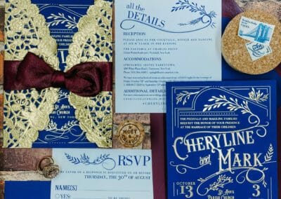 navy blue wedding invitation with gold foil imprinting - features vintage inspired design with ornate embellishments and typography. Invitation is wrapped in gold doily.