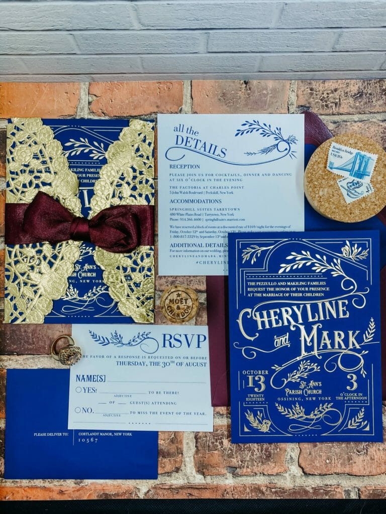 navy blue wedding invitation with gold foil imprinting - features vintage inspired design with ornate embellishments and typography. Invitation is wrapped in gold doily.